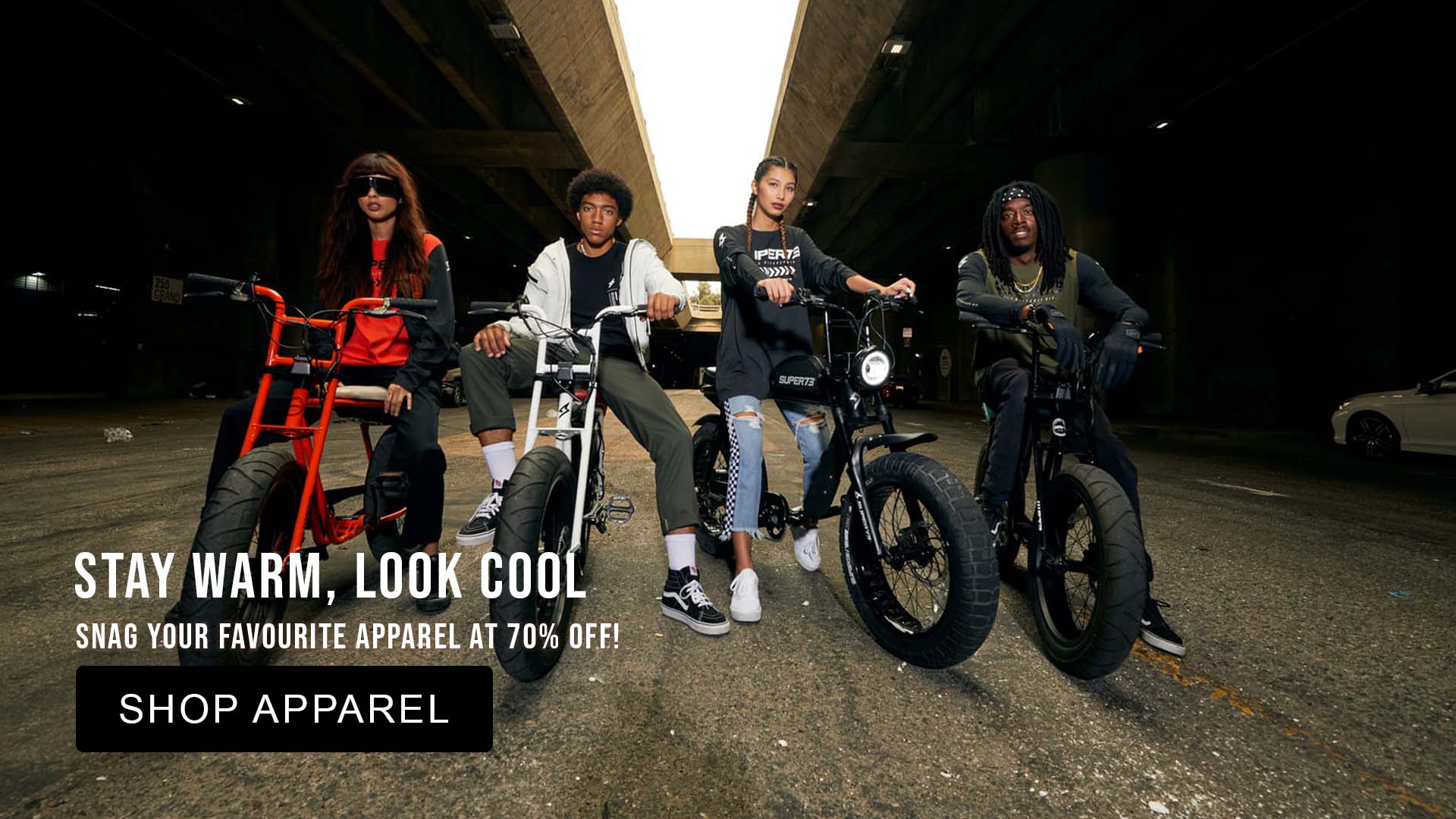 Four people on fat-tire bikes in a dark tunnel with Super73 Apparel promotional text overlay.