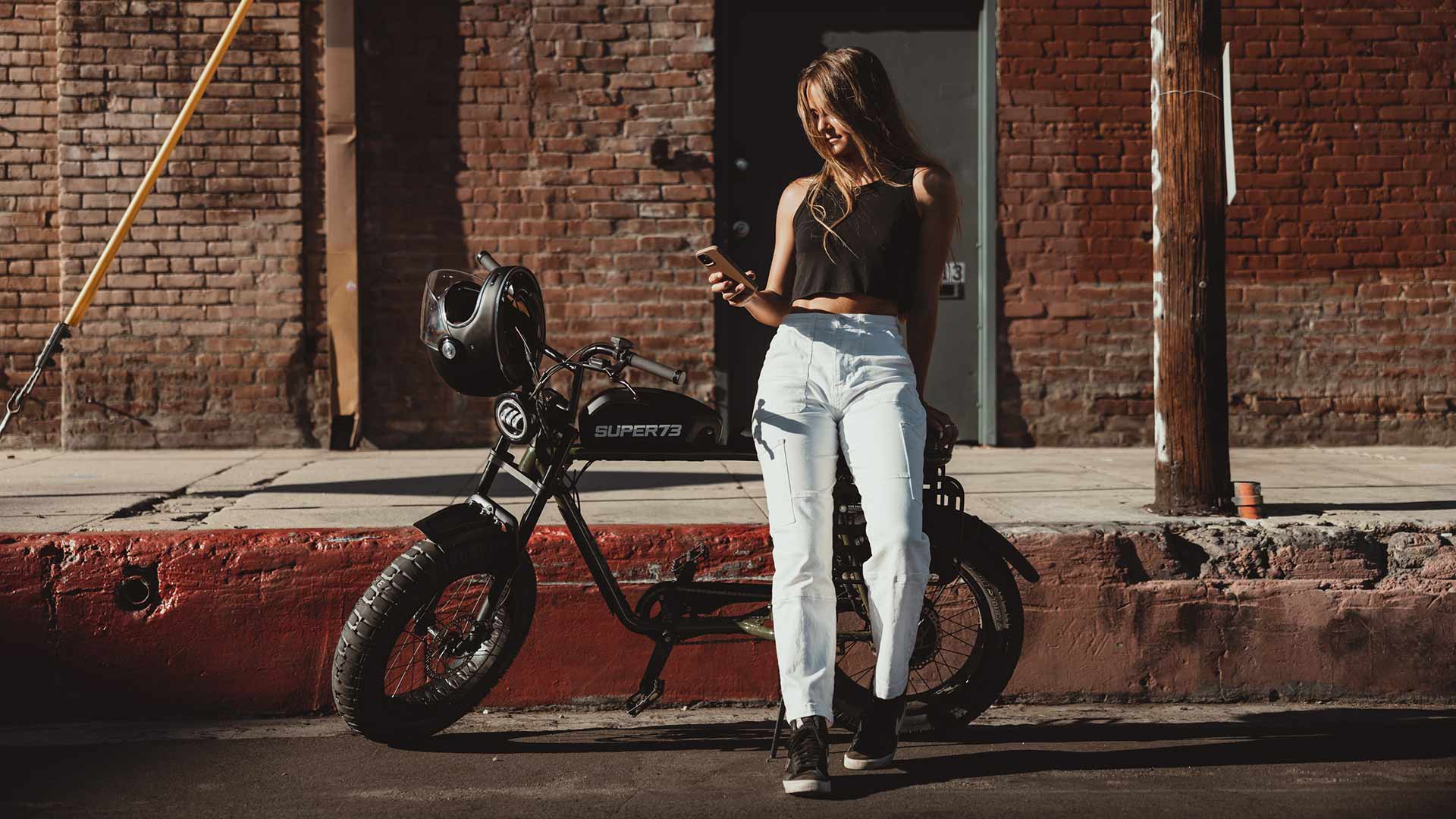 Rider standing next to Super73 ebike while checking the mobile app for torque updates